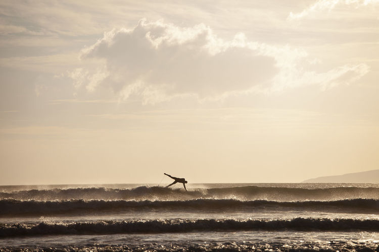 Silhouette man falling while surfing in sea against sky during sunset