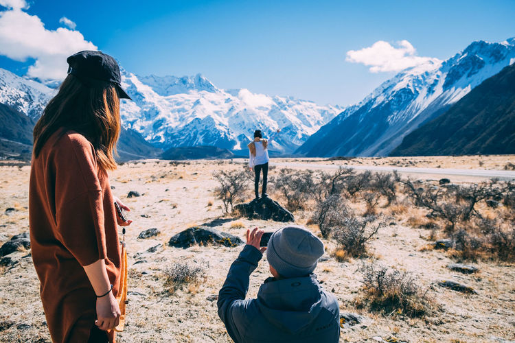 Rear view of woman photographing on snowcapped mountains against sky