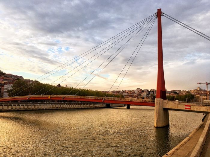 View of suspension bridge over river against cloudy sky