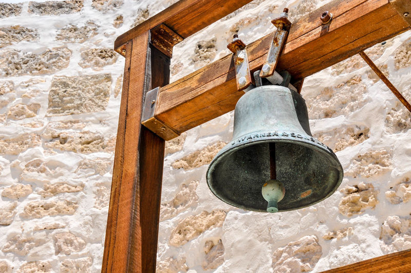 Low angle view of bell on wood against stone wall