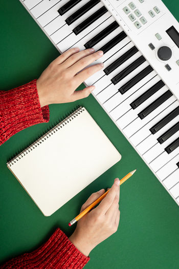 Female hands, blank notepad and music keys on a green background, top view.
