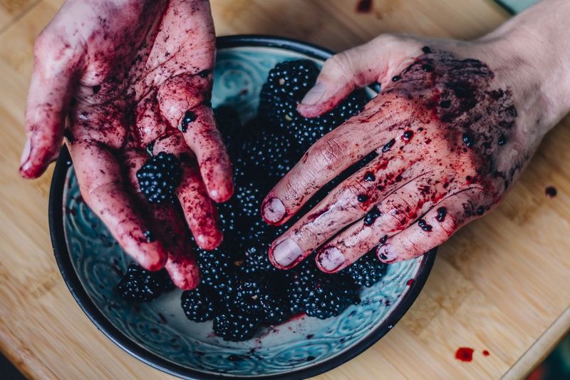Cropped image of dirty hands holding blackberries in plate
