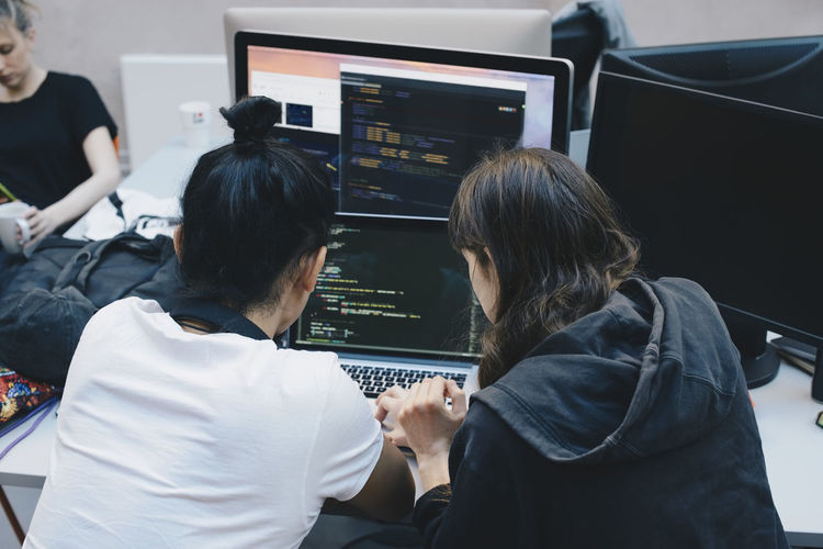 Over the shoulder view of computer programmers using laptop at office desk