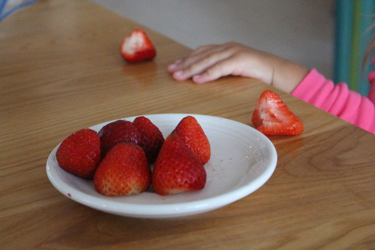 Cropped hand by strawberries on dinning table at home