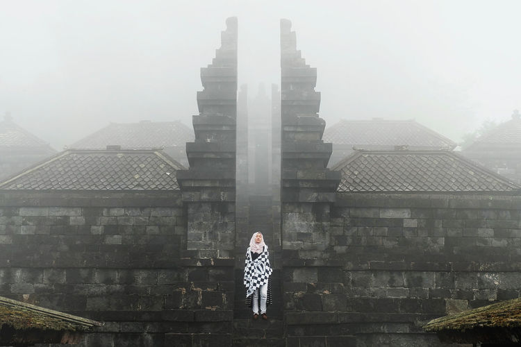 Woman standing against temple during foggy weather