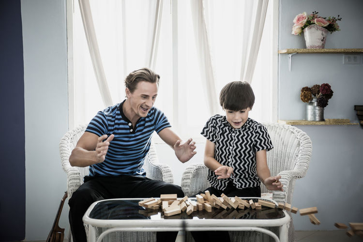 Father and son with toy blocks collapsing on table at home