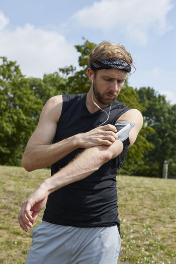 Man listening music while exercising against trees