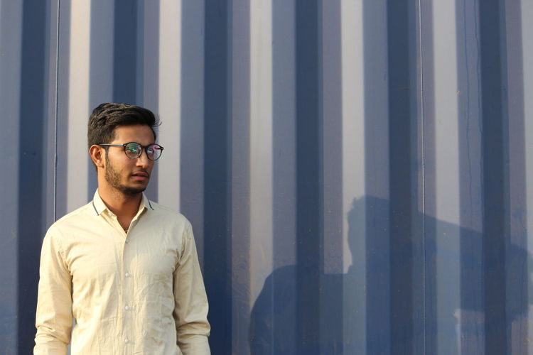 Young man wearing eyeglasses standing against wall