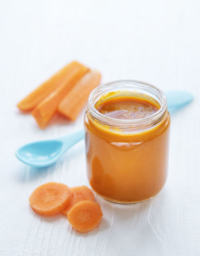 Baby carrot mashed with spoon in glass jar, baby food