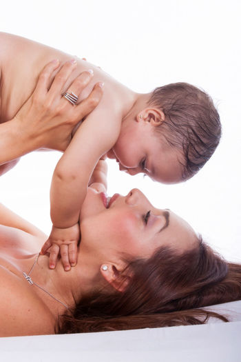Mother lifting shirtless daughter against white background