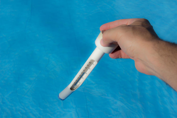 Cropped hand holding thermometer in swimming pool during sunny day