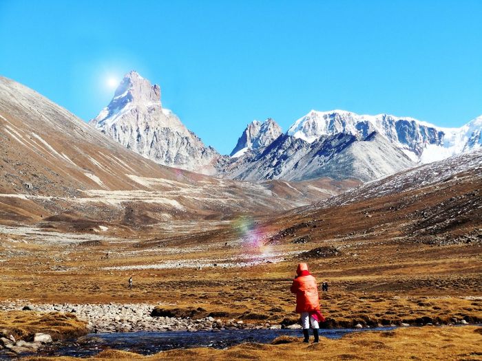 Rear view of person standing on landscape by snowcapped mountains against sky