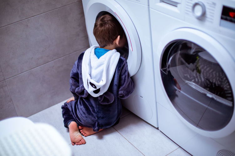 Rear view of boy peeking in washing machine