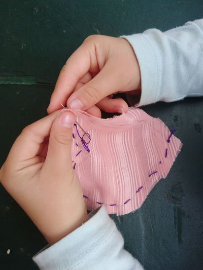 Cropped hands of child stitching fabric on table