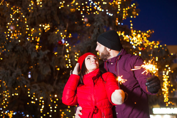 Couple embracing while holding sparkler against illuminated tree