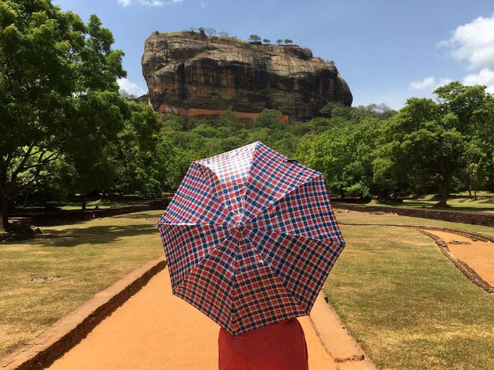 A visitor holds an umbrella in sigiriya rock fortress. rear view of woman on field against sky. 