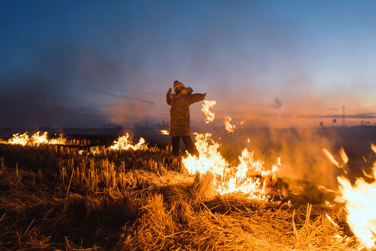 Woman standing amidst fire on land against sky