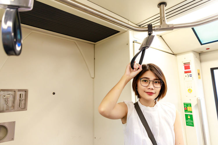 Asian young short hair beautiful woman wearing glasses holding handle grip while moving in the train