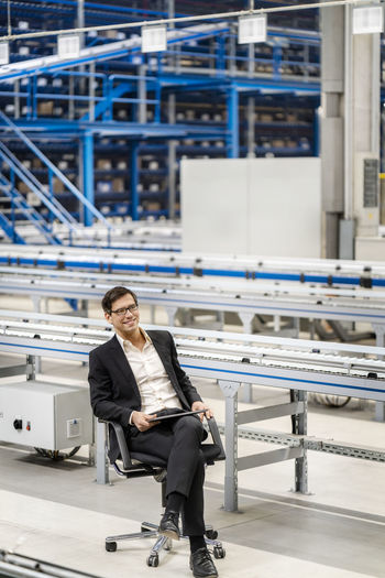 Mature businessman with legs crossed at knee in factory