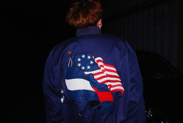 Rear view of man wearing jacket with american flag print against black background