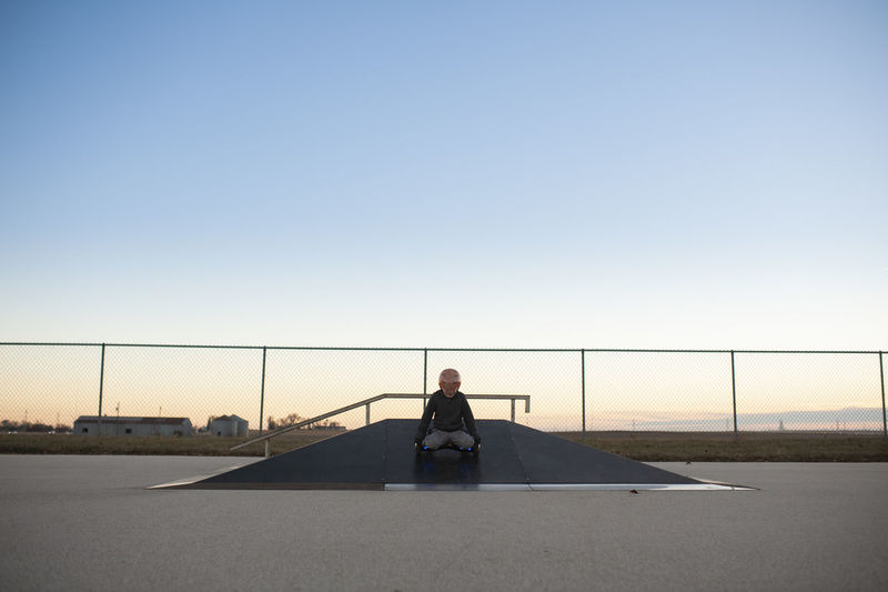 Centered image of boy comping down ramp at skate park on knees