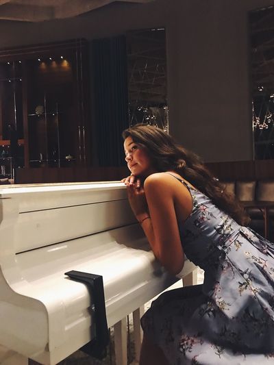 Young woman looking away leaning against grand piano at restaurant