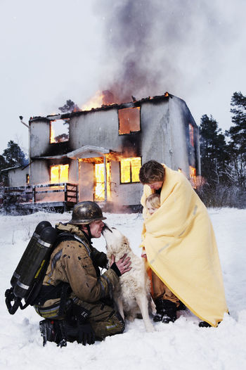 Fireman with rescued people and dog in front of burning house