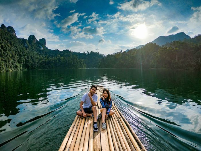 Couple sitting on wooden raft in lake against trees