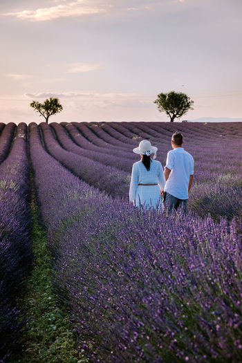 Rear view of couple standing on flowering field against sky