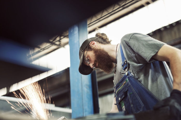Low angle view of blue collar worker using welding machine in steel industry