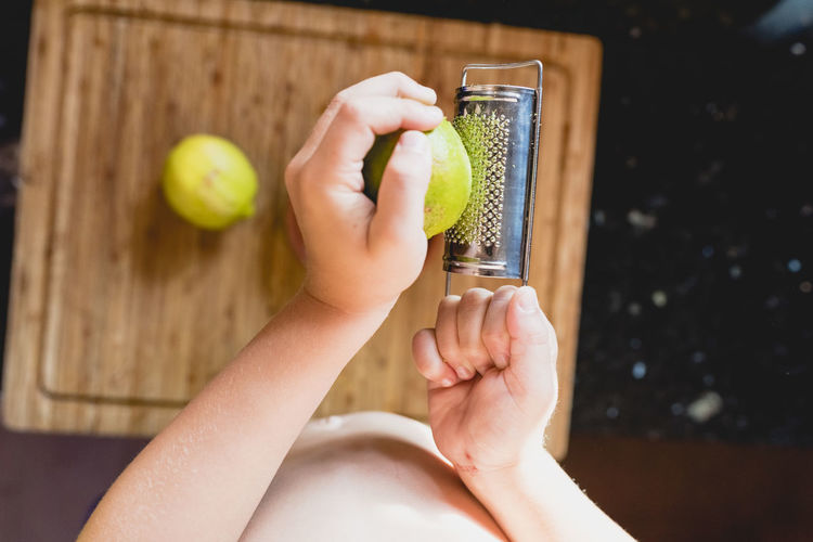 Midsection of shirtless child grating lemon at table