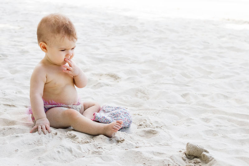 Cute little baby girl in pink swimming trunks playing sand at beach. sensory development for kids. 