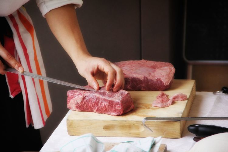 Cropped image of chef cutting beef in kitchen