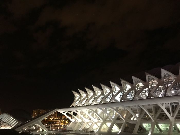 Low angle view of illuminated bridge against buildings at night