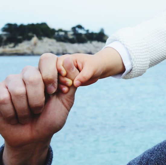 Close-up of cropped father holding daughter hand against sea