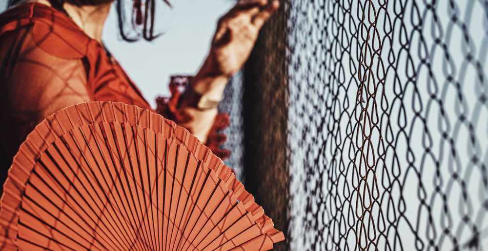 Midsection of woman holding hand fan by chainlink fence