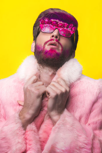 Handsome young man wearing sunglasses and fur coat against yellow background