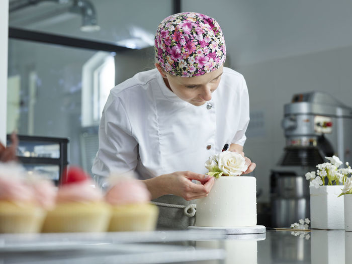 Young confectioner decorating cake with marzipan roses in kitchen