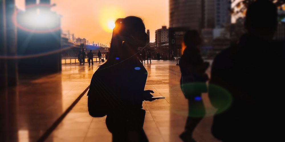 Silhouette woman with umbrella walking in city during sunset