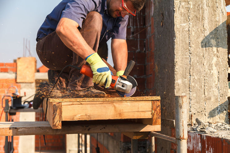 Male carpenter cutting wood with circular saw at construction site
