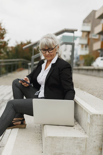 WOMAN USING MOBILE PHONE WHILE SITTING ON LAPTOP