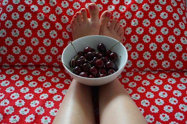 Low section of woman with cherries in bowl sitting at home