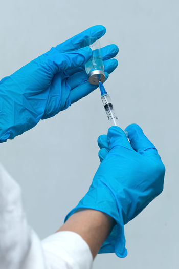 Cropped hands of scientist holding syringe with vial against wall
