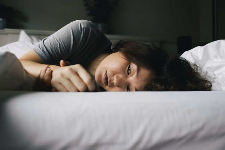 Tired woman suffering from mental health disorder lying on bed alone at home