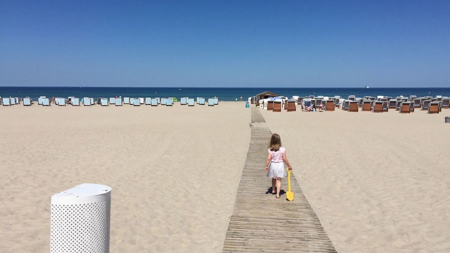 Rear view of girl walking on boardwalk at sandy beach