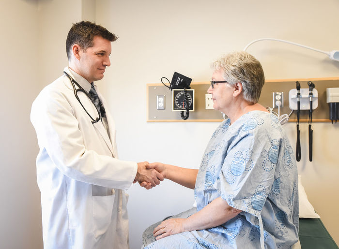 Doctor shaking hands with older patient wearing gown in clinic.