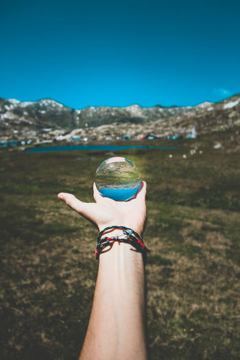 Cropped hand holding crystal ball against land