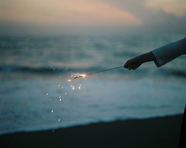 Close-up of hand holding fishing rod over sea