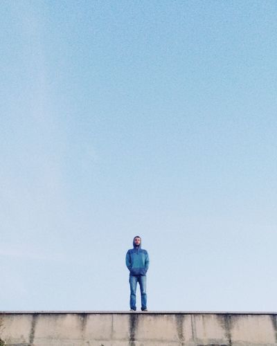 Low angle view of man standing on surrounding wall against sky