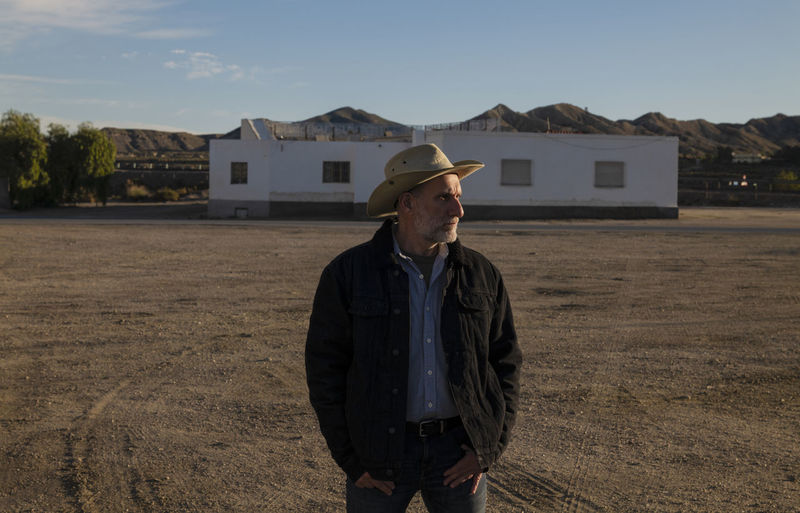 Adult man in cowboy hat standing in front of white building